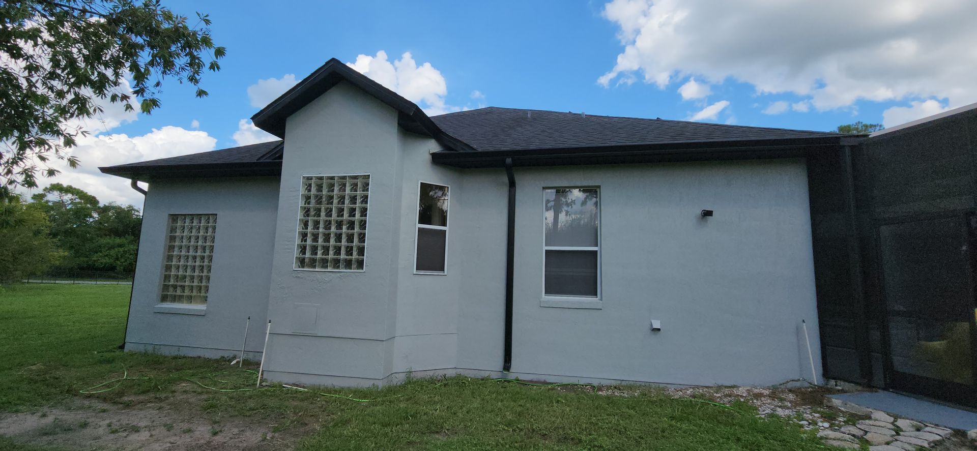 A white house with a black roof is sitting on top of a lush green field.