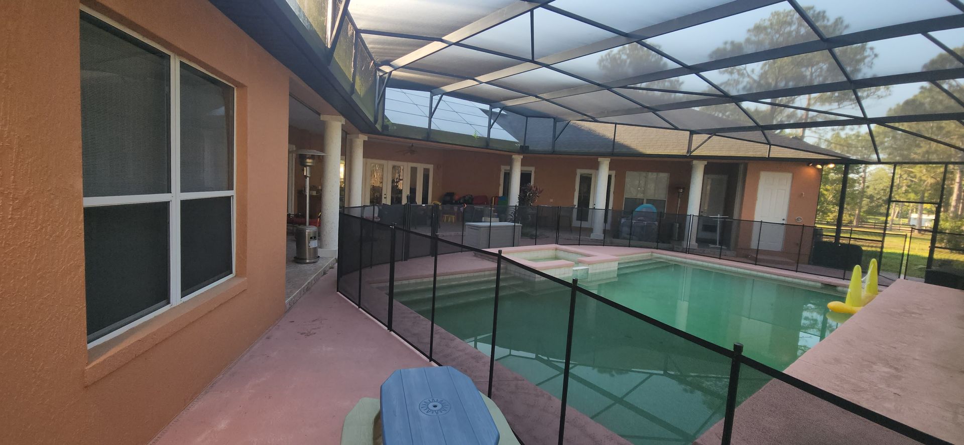 A large swimming pool in the backyard of a house with a fence around it.