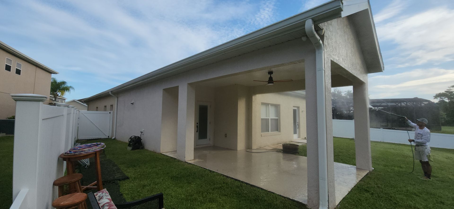 A man is spraying a house with a hose in a backyard.