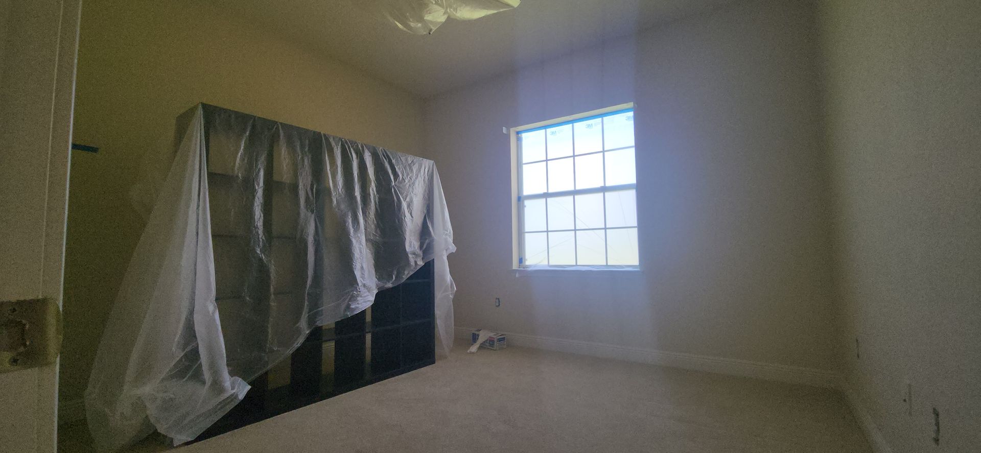 An empty room with a window and a bed covered in plastic.