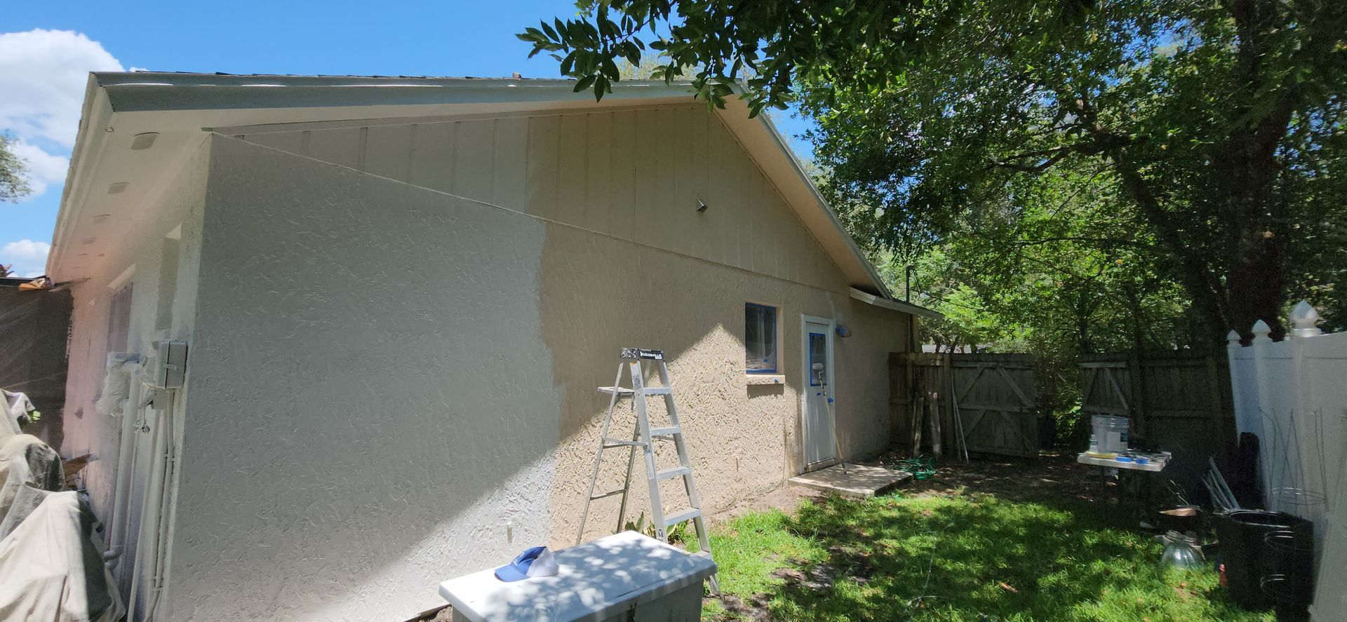 The backyard of a house with a covered patio and a large lawn.