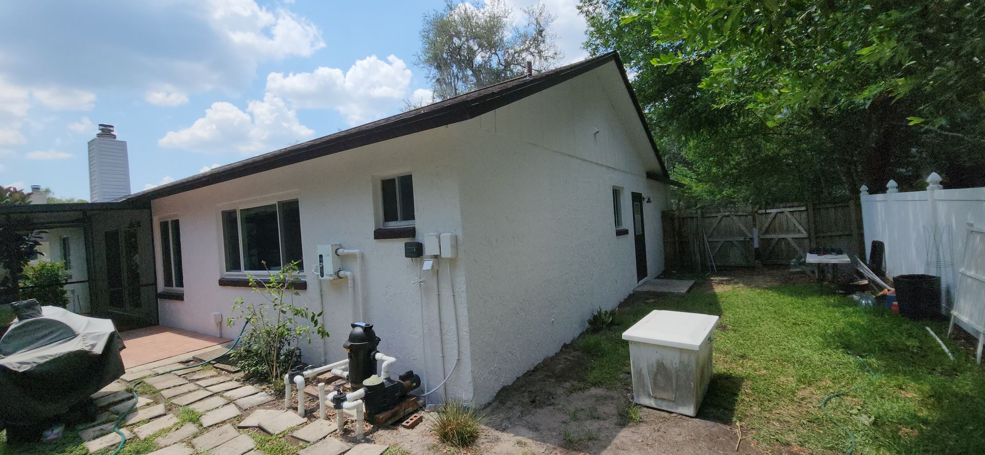 The back of a house with a covered porch and a white fence.