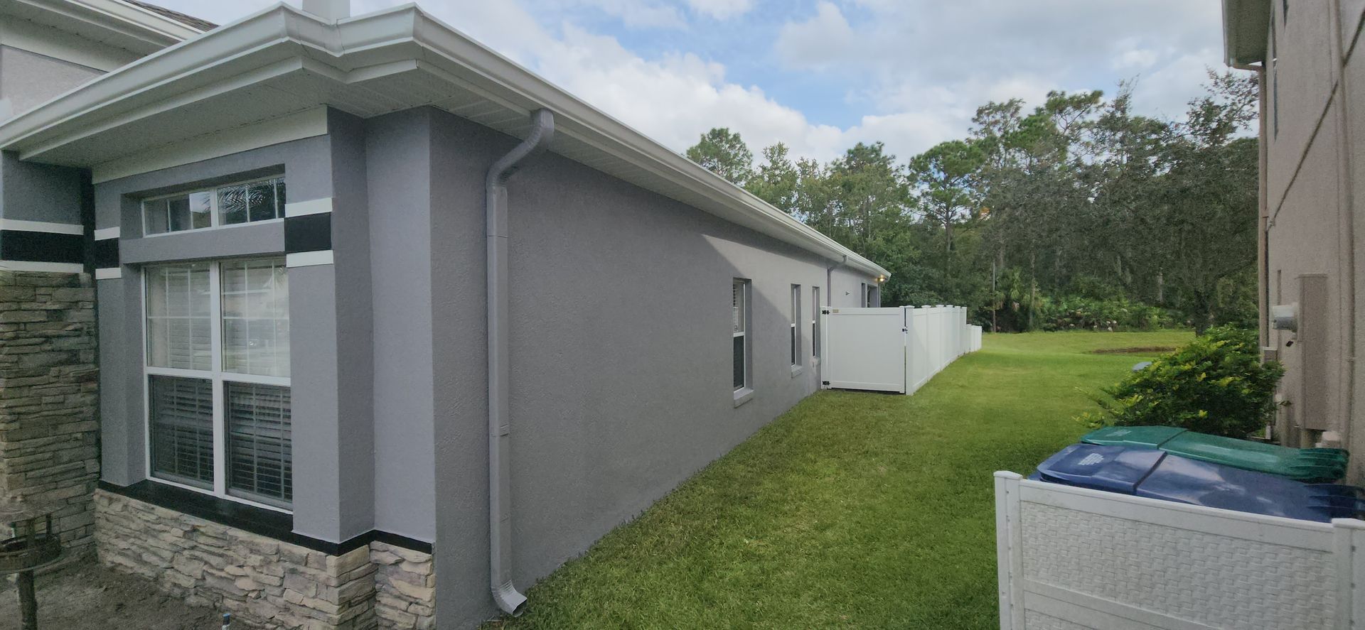 The side of a house with a white fence in the backyard.