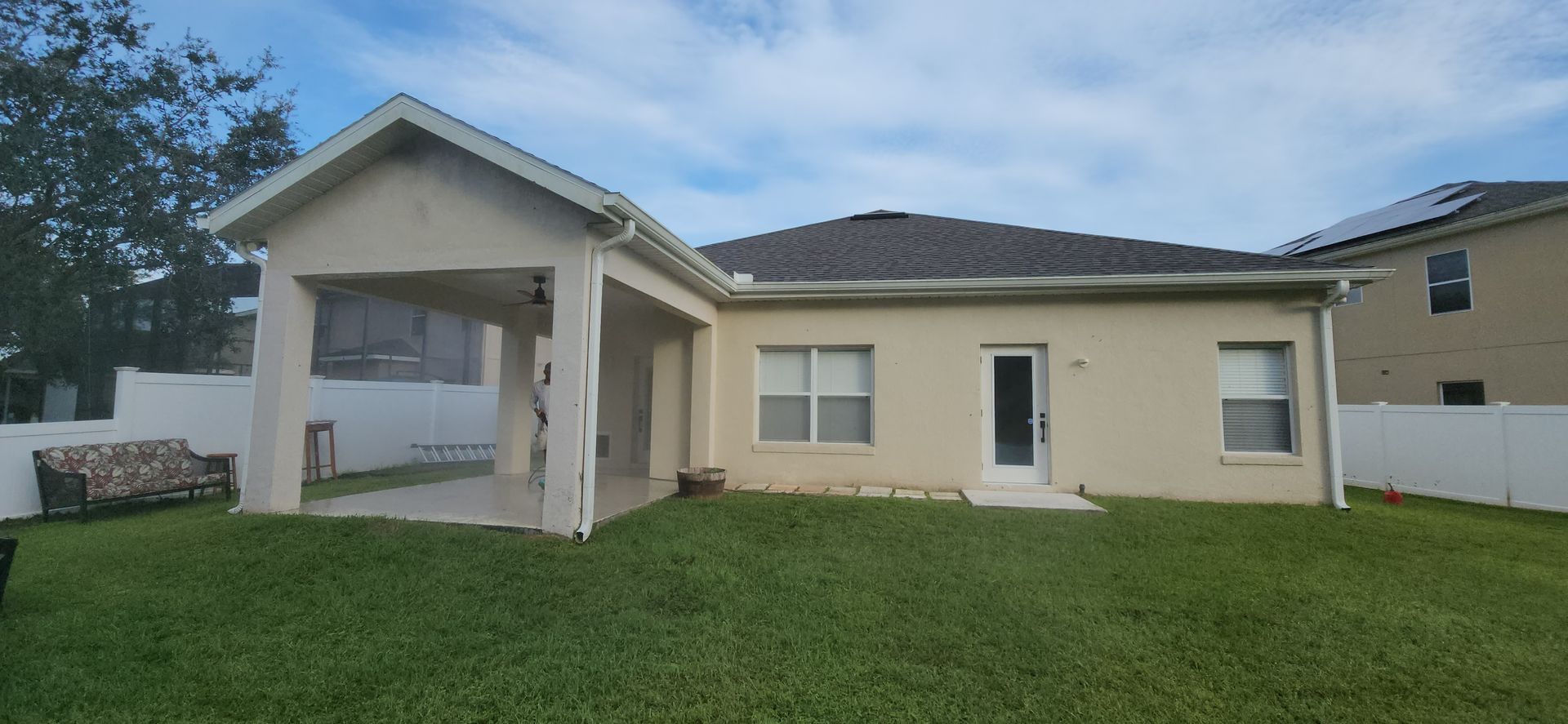 The backyard of a house with a covered patio and a large lawn.